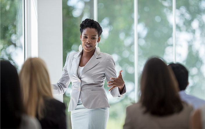 An African American woman in business professional attire is presenting to a group.