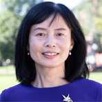 Amy Zeng of Suffolk University, with black side-parted shoulder length hair, almond-shaped dark brown eyes, pale complexion, and friendly smile, and wearing a deep blue high-neckline blouse. She stands outside with trees and sunny day in the background.